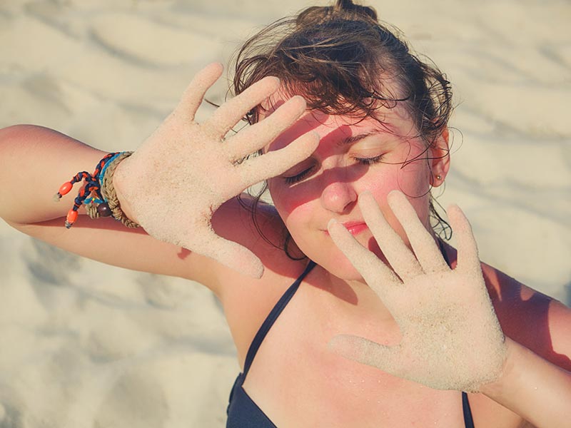 jonge vrouw met roodverbrand gezicht kijkt in de zon met handen voor haar ogen